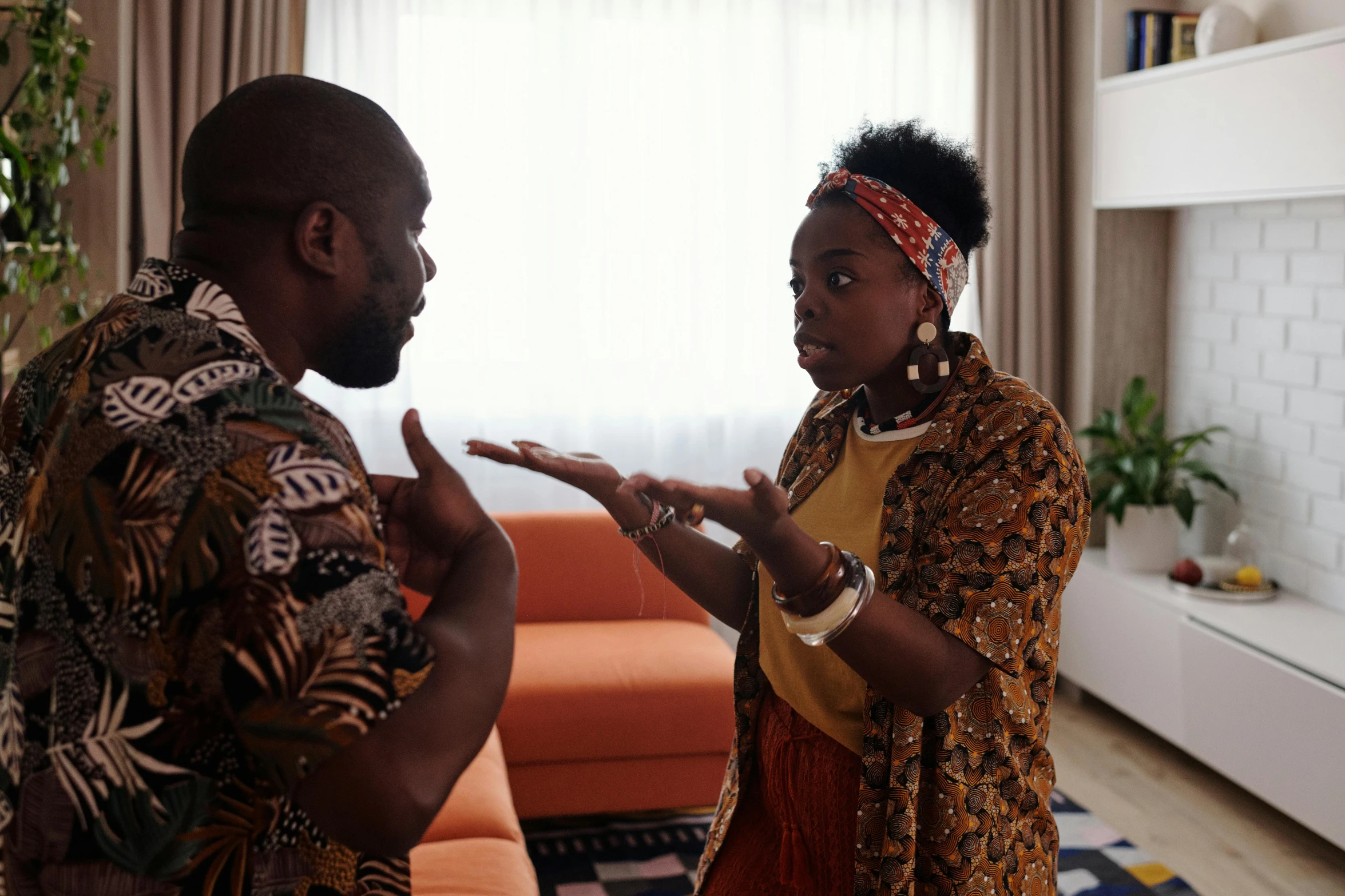 a man and a woman standing in a living room, by Ingrida Kadaka, pexels contest winner, afrofuturism, royal family during an argument, in orange clothes) fight, patterned clothing, commercial