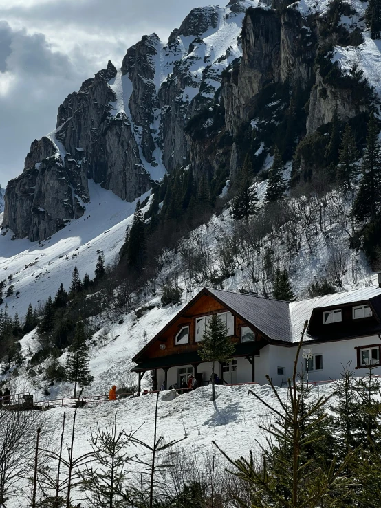 a group of people riding skis down a snow covered slope, house on a hill, photo of džesika devic, cozy place, craggy mountains