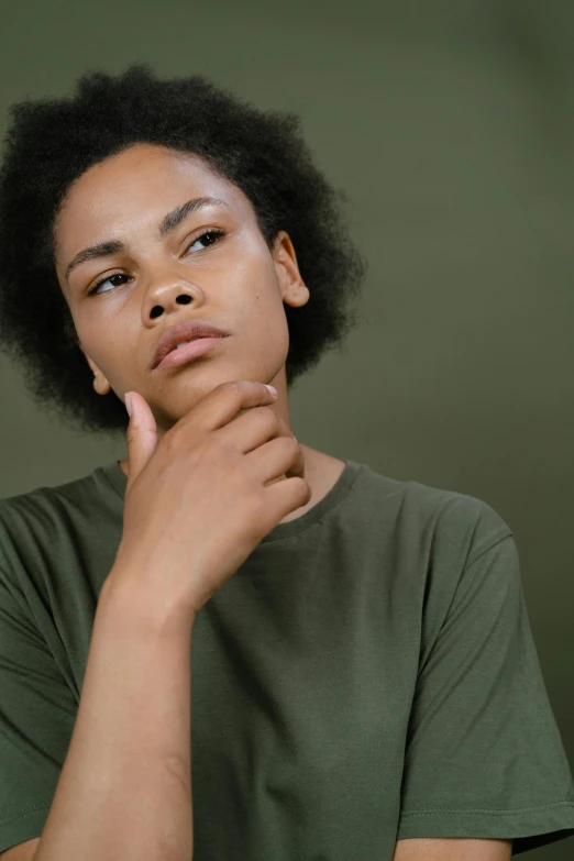 a close up of a person with a hand on their chin, by Lily Delissa Joseph, muted green, looking confused, casual pose, black young woman