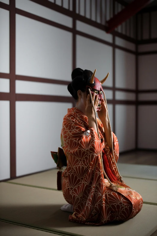 a woman sitting on a mat talking on a cell phone, a picture, inspired by Otake Chikuha, unsplash, wearing a noh theatre mask, square, evil pose, wearing kimono armour