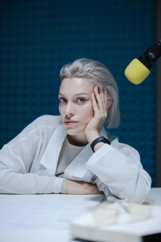 a woman sitting at a table in front of a microphone, by artist, trending on reddit, antipodeans, pale hair, high quality photo, thinker pose, studio portrait