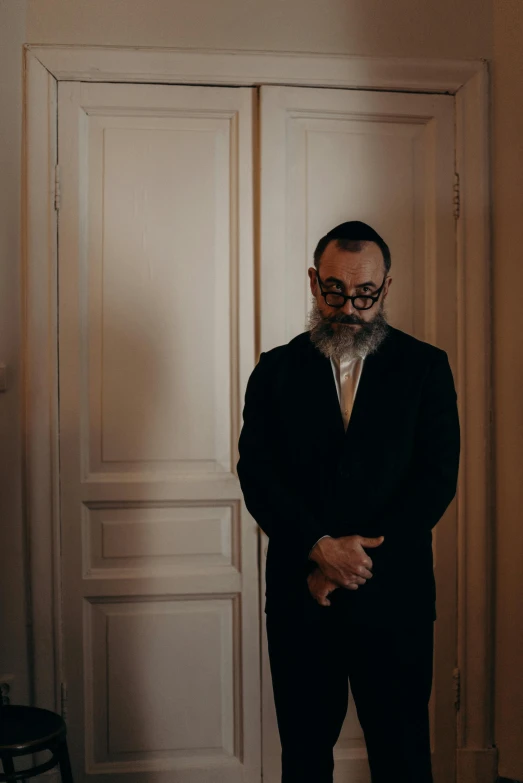 a man in a suit standing in front of a door, alessio albi, circle beard, doing a prayer, lgbtq