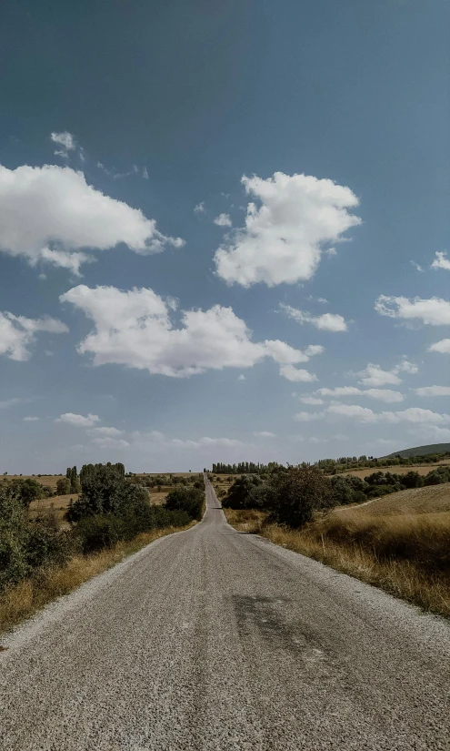 a man riding a motorcycle down a dirt road, an album cover, by Jessie Algie, unsplash contest winner, panorama view of the sky, turkey, today\'s featured photograph 4k, peaceful puffy clouds