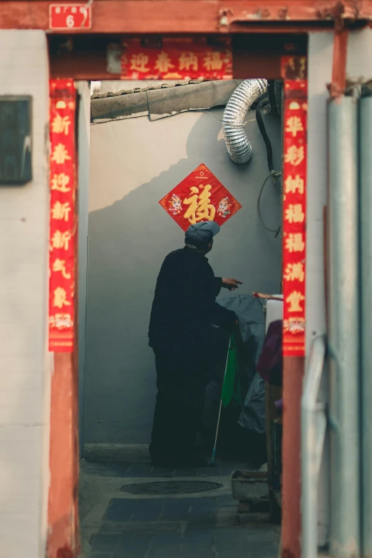 a man standing in the doorway of a building, a silk screen, by Shang Xi, pexels contest winner, symbolism, holding a holy symbol, old woman, colorful signs, low quality photo