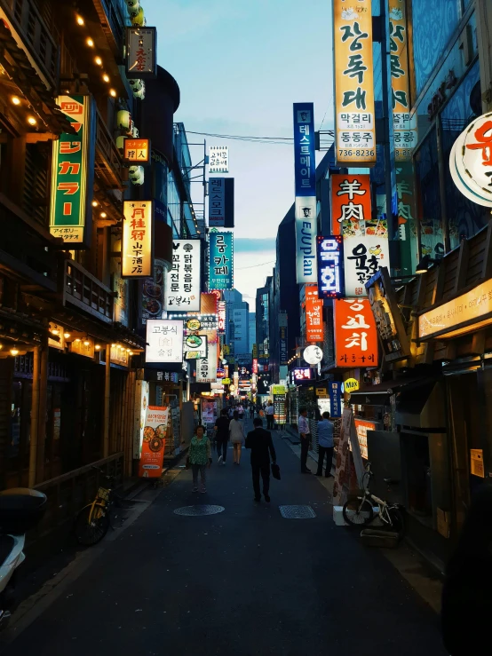 a group of people walking down a street next to tall buildings, by Jang Seung-eop, trending on unsplash, few neon signs, ancient city streets behind her, square, korean supper