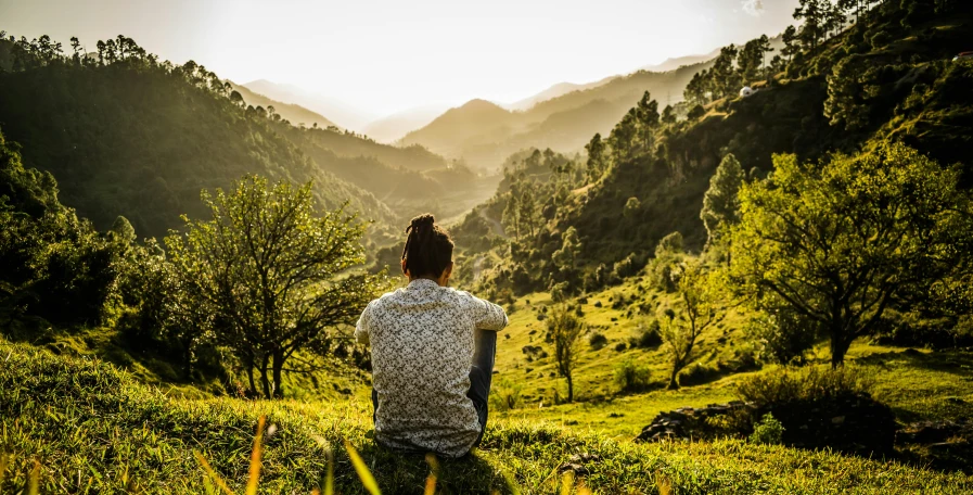 a man sitting on top of a lush green hillside, by Julia Pishtar, pexels contest winner, young himalayan woman, psychedelic therapy, facing away, late afternoon