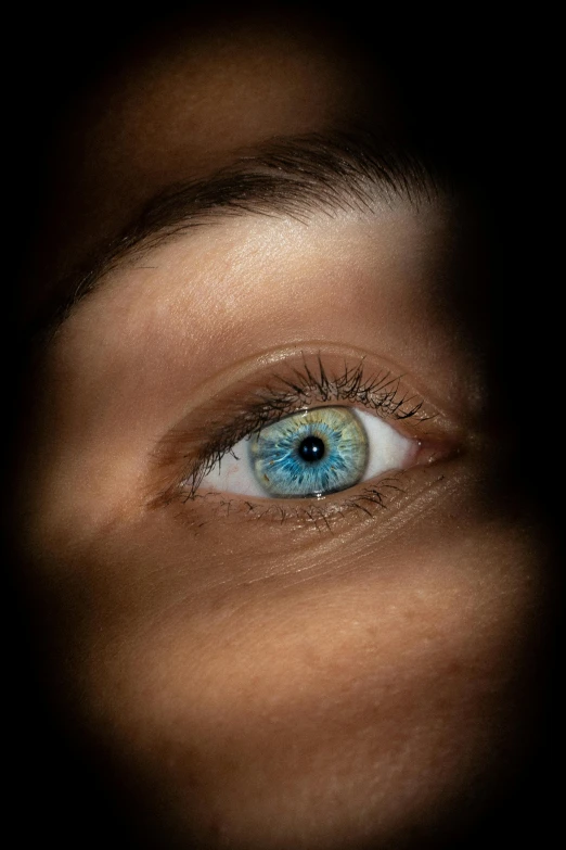 a close up of a person's blue eye, an album cover, inspired by Elsa Bleda, trending on pexels, with a black background, heterochromia, spying discretly, high angle shot