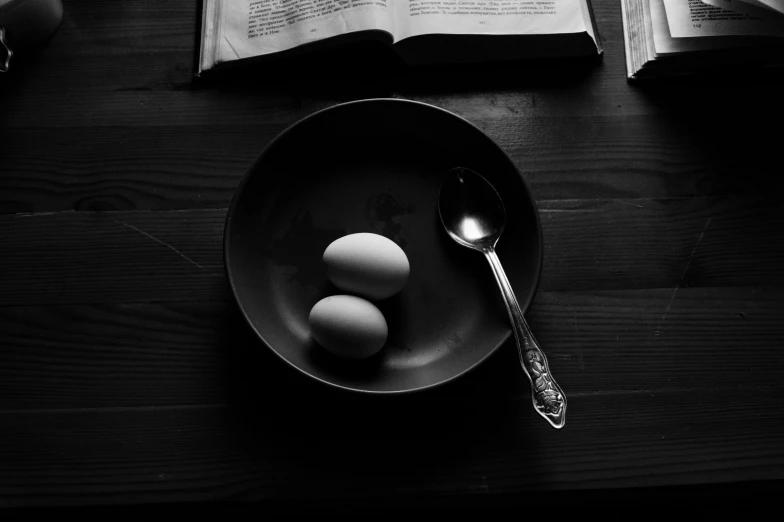 a bowl of eggs sitting on top of a wooden table, a black and white photo, by Karl Buesgen, unsplash, realism, orthodox, the fork is on a plate, reading, in a dark