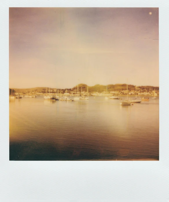 a group of boats floating on top of a body of water, a polaroid photo, gradient white to gold, harbour in background, sunfaded, bay
