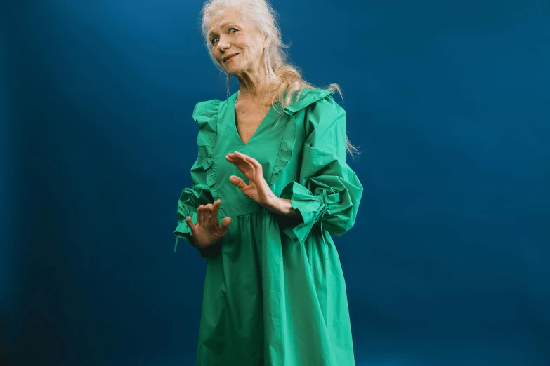 a woman in a green dress on a blue background, inspired by Grethe Jürgens, pexels contest winner, an elderly, still from a music video, vivienne westwood, nina masic