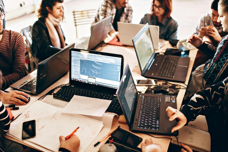 a group of people sitting around a table with laptops, by Carey Morris, pexels, engineering, intricated, 9 9 designs, excel running on the computer