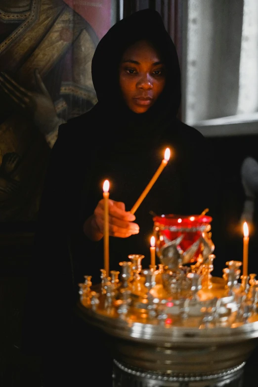 a woman is lighting candles in a church, aida muluneh, highlight, grey, university