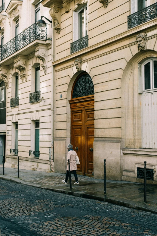 a woman is walking down a cobblestone street, trending on unsplash, paris school, tall door, architectural digest, brown, neoclassic