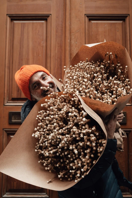 a person holding a bunch of flowers in front of a door, inspired by Ai Weiwei, trending on pexels, waxed beard, seeds, winter season, philippe starck