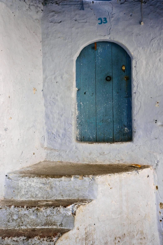 a blue door sitting on the side of a white building, inspired by Alberto Morrocco, cave entrance, rustic, square, nubian