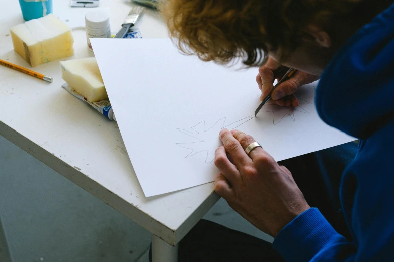 a woman is drawing on a piece of paper, a drawing, inspired by Brett Whiteley, process art, on a white table, holly herndon origami statue, in a workshop, white tracing