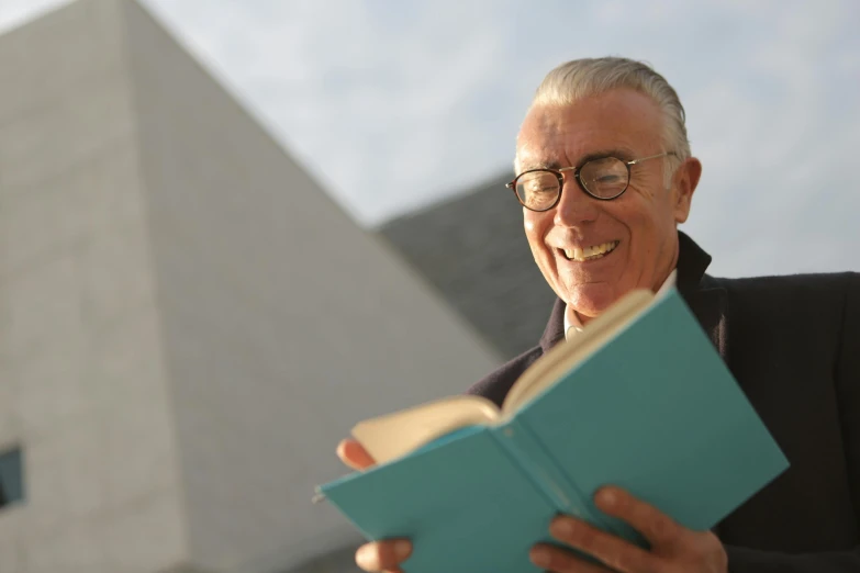 a man reading a book in front of a building, inspired by Buckminster Fuller, academic art, subject is smiling, profile image, calatrava, wearing square glasses