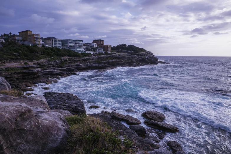 a large body of water next to a rocky shore, pexels contest winner, australian tonalism, purple roofs, bondi beach in the background, geological strata, goodnight