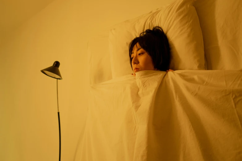 a woman laying in bed under a blanket, inspired by Elsa Bleda, unsplash, hyperrealism, japanese live-action movie, yellow light, emerging from her lamp, 奈良美智