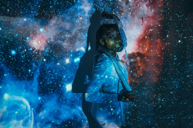 a woman standing in front of a galaxy background, pexels contest winner, afrofuturism, projection mapping, young thug, emerging from blue fire, man in silver space suit