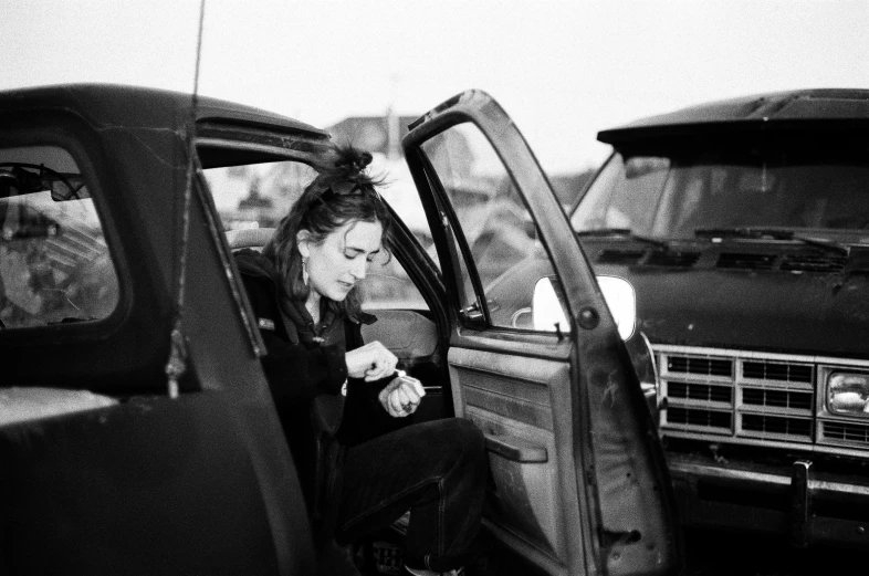 a black and white photo of a woman sitting in a car, by Thomas Fogarty, tumblr, auto-destructive art, winona ryder, junk yard, checking her cell phone, twilight junkyard