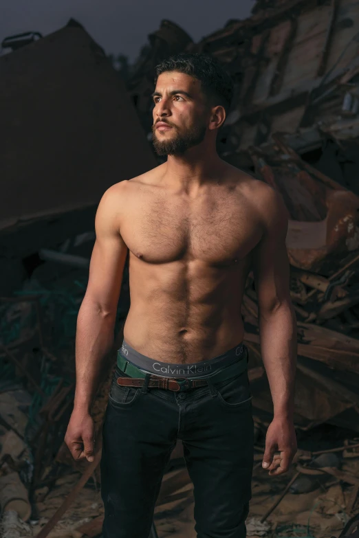 a shirtless man standing in front of a pile of rubble, a colorized photo, inspired by Volkan Baga, pexels contest winner, masculine and handsome, physical : tinyest midriff ever, portrait of danny gonzalez, indoor picture