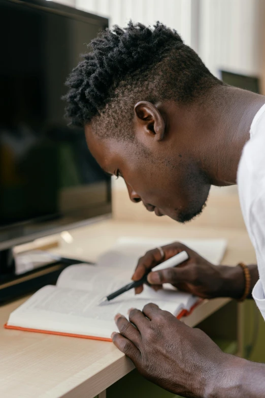 a man sitting at a desk writing on a piece of paper, pexels contest winner, academic art, adut akech, book library studying, hair styled in a bun, thumbnail