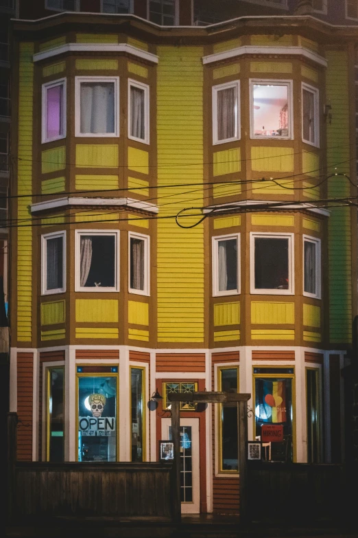 a yellow and green building sitting on the side of a road, inspired by Wes Anderson, pexels contest winner, art nouveau, taverns nighttime lifestyle, chile, bay window, multi colored