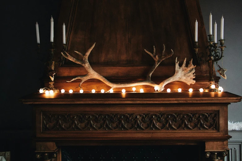 a fireplace with candles and antlers on top of it, inspired by Elsa Bleda, pexels contest winner, arts and crafts movement, carved wood, elk, curated collection, low - lighting