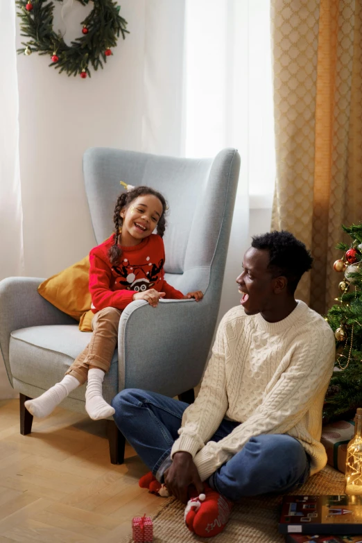 a man and a little girl sitting in front of a christmas tree, comfy chairs, diverse, grey, kano)