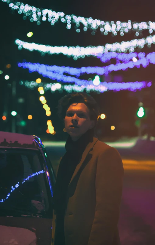 a man standing next to a parked car at night, an album cover, unsplash, orelsan, portait photo, cozy lights, cold color