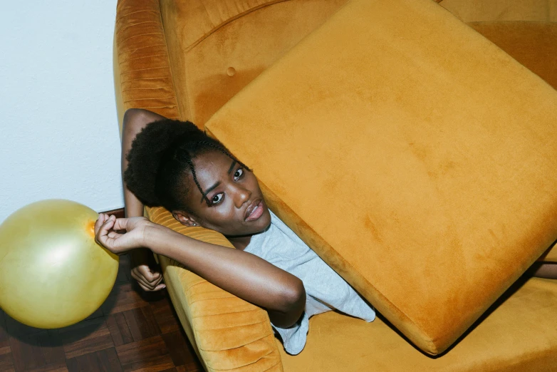 a woman sitting on a couch holding a balloon, inspired by Elsa Bleda, pexels contest winner, brown skin like soil, yellow carpeted, ignant, velvet couch