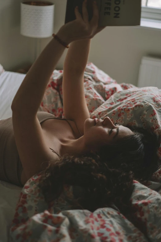 a woman laying in bed reading a book, a polaroid photo, inspired by Elsa Bleda, trending on pexels, happening, armpit, looking at his phone, curly haired, gif