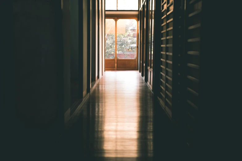 a hallway leading to a large window in a building, inspired by Elsa Bleda, pexels contest winner, light and space, hardwood floors, private school, golden hours, rows of doors