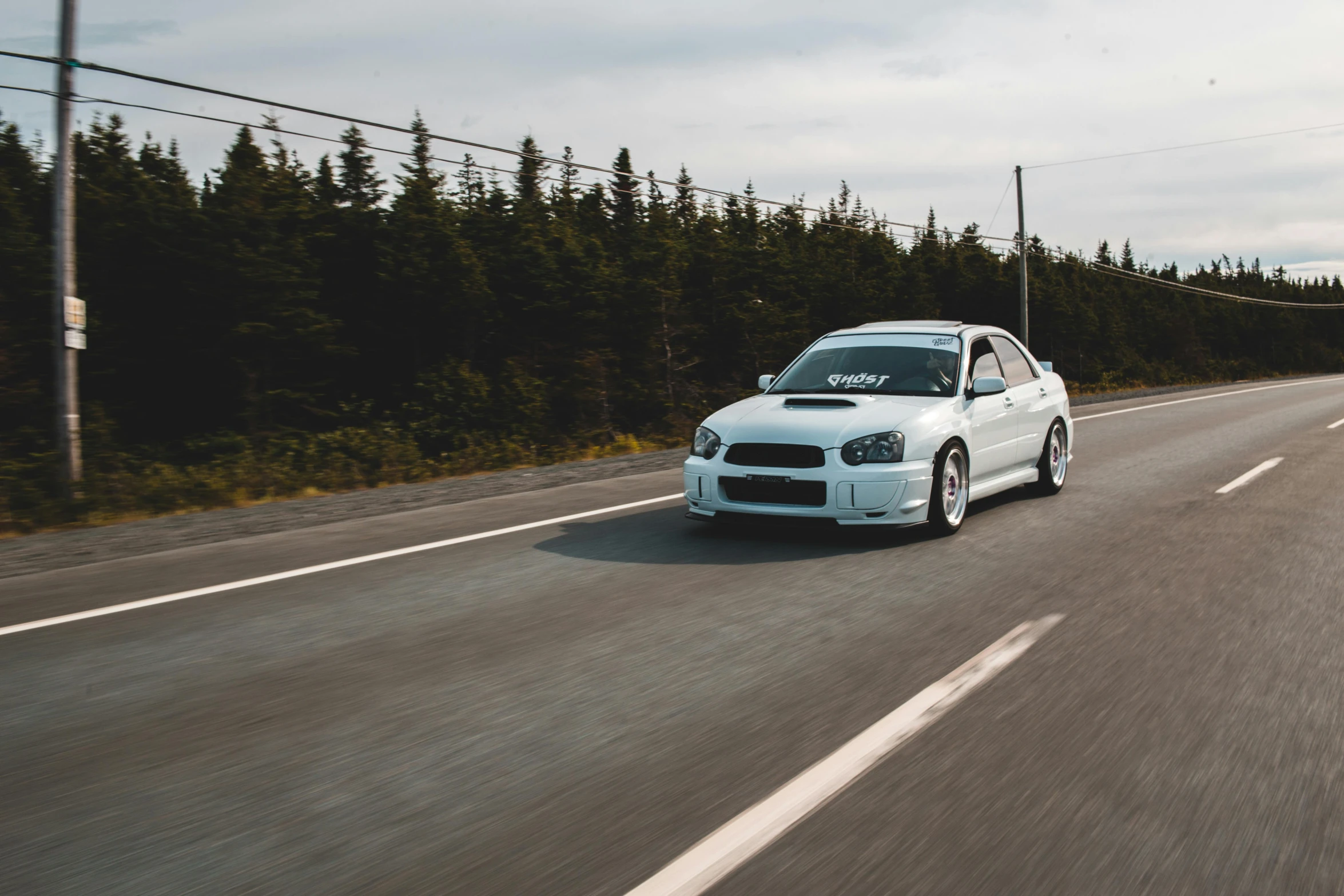 a white car driving down a road next to a forest, by Brian Snøddy, hurufiyya, on a street race track, profile pic, subaru, slim build