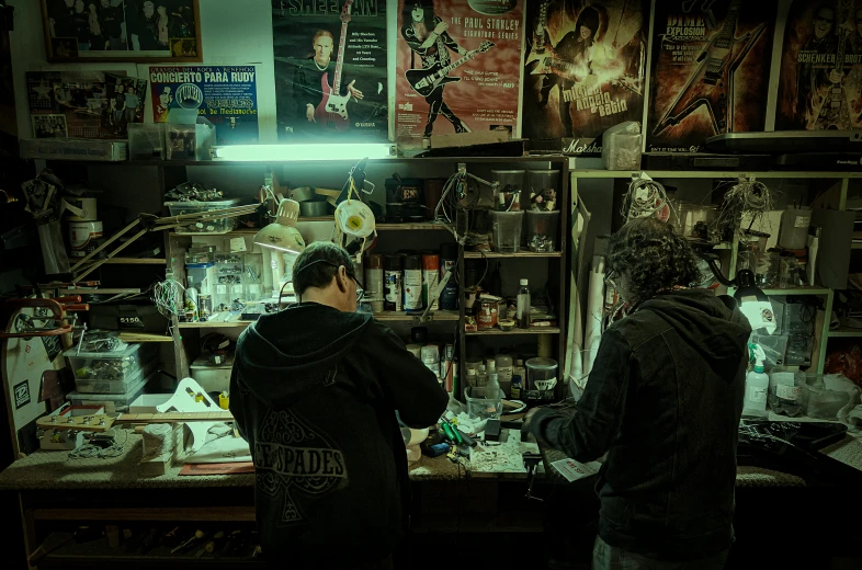 a couple of men standing next to each other in a room, an airbrush painting, by Elsa Bleda, pexels contest winner, process art, shop window for magical weapons, workbench, busy night, weta workshop