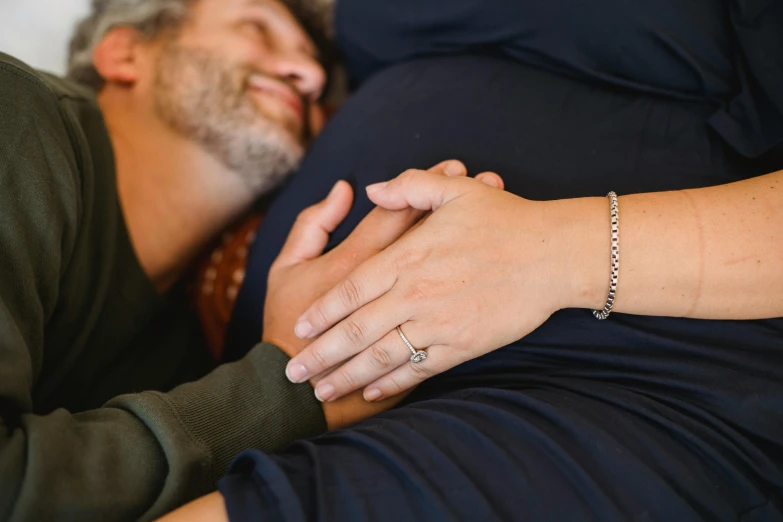 a man and a woman laying next to each other, pregnant belly, wearing two silver bracelets, profile image, thumbnail