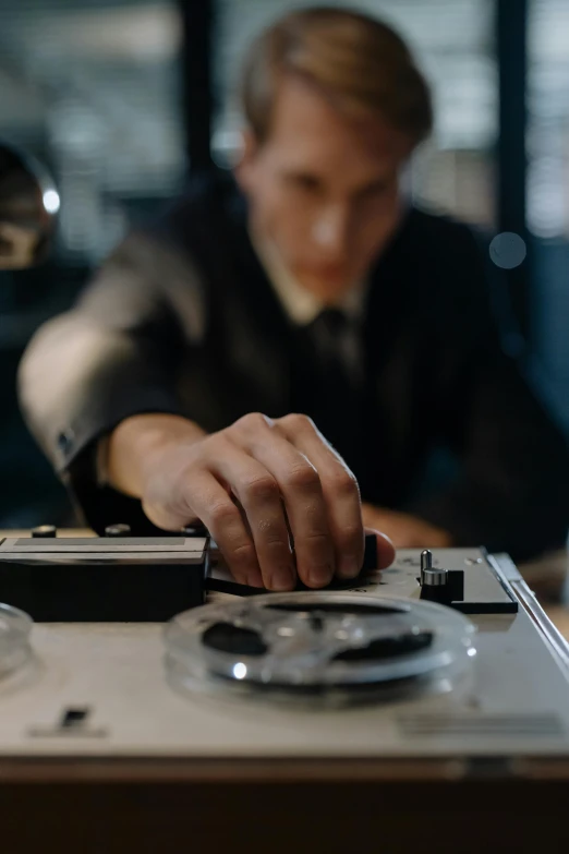 a man sitting at a desk working on a computer, an album cover, inspired by Oskar Lüthy, unsplash, scientific equipment, medium close - up ( mcu ), hasselblad, elegantly dressed