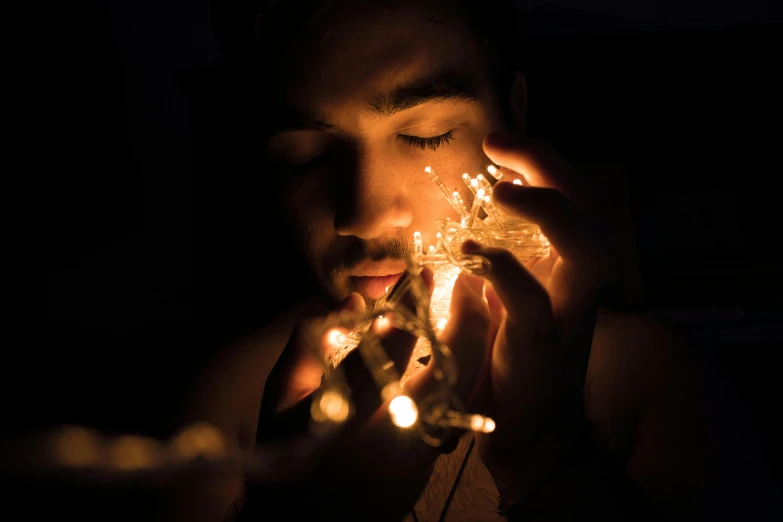 a man holding a string of lights in his hands, by Adam Marczyński, pexels contest winner, hyperrealism, pensive expression, crystal lights, light skin, close-up shoot