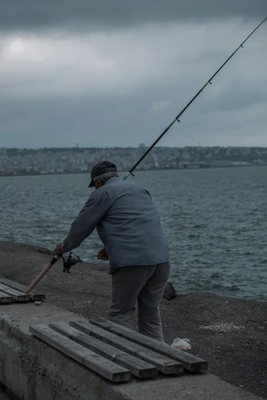 a man standing on top of a pier next to a body of water, fishing pole, photo of zurich, old man doing hard work, movie footage