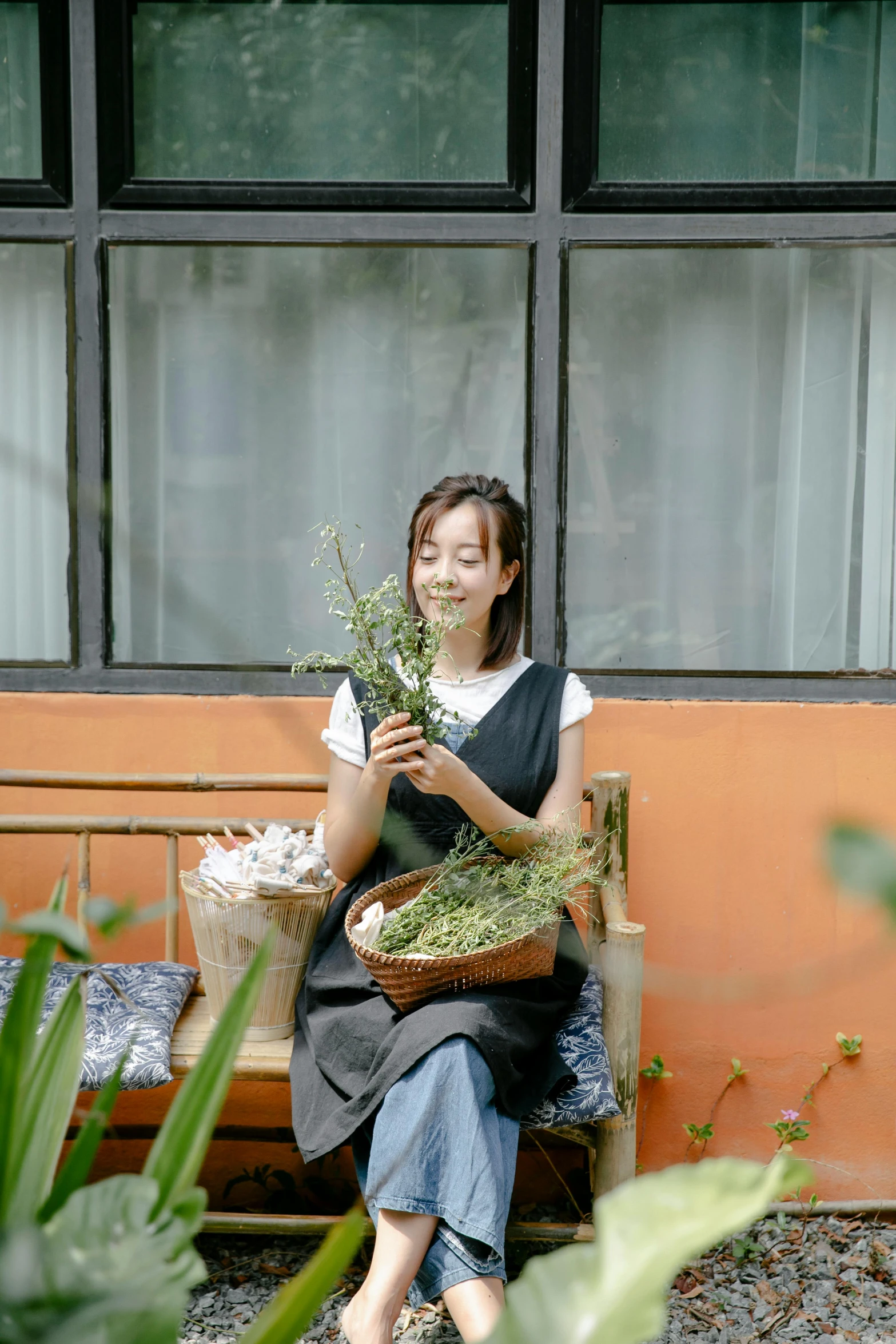 a woman sitting on a bench holding a basket of flowers, inspired by Cui Bai, unsplash, process art, dried herbs, taiwan, in a garden of a house, wearing an apron