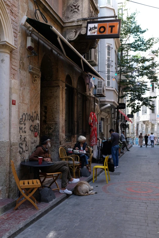 a group of people sitting outside of a building, street art, narrow and winding cozy streets, fallout style istanbul, in a sidewalk cafe, daniel libeskind