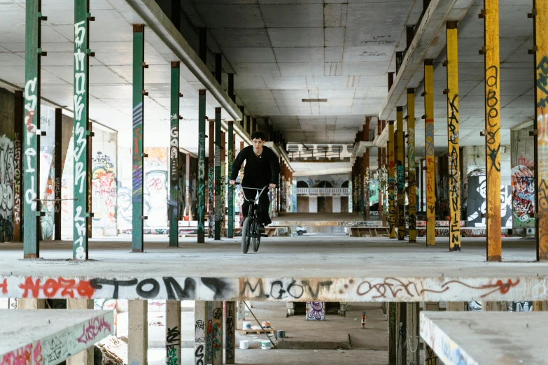 a person riding a bike in an abandoned building, by Matthias Stom, unsplash, graffiti, bjarke ingels, dwell, at a skate park, tom bangshaw