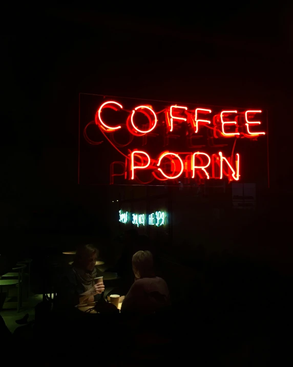 a couple of people sitting at a table in front of a neon sign, inspired by Nan Goldin, trending on unsplash, full of steaming coffee, /r/earthporn, lewd, seen from outside