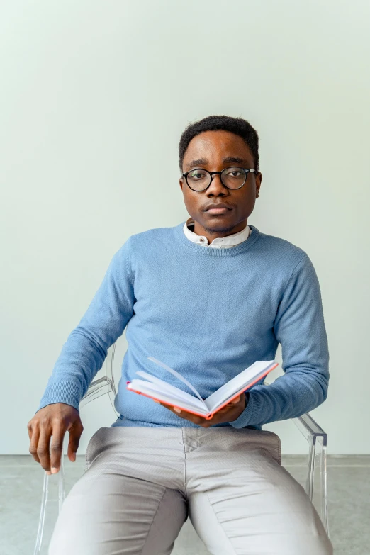 a woman sitting in a chair reading a book, inspired by Stokely Webster, pexels contest winner, african man, wearing a light blue shirt, nerd, proud serious expression