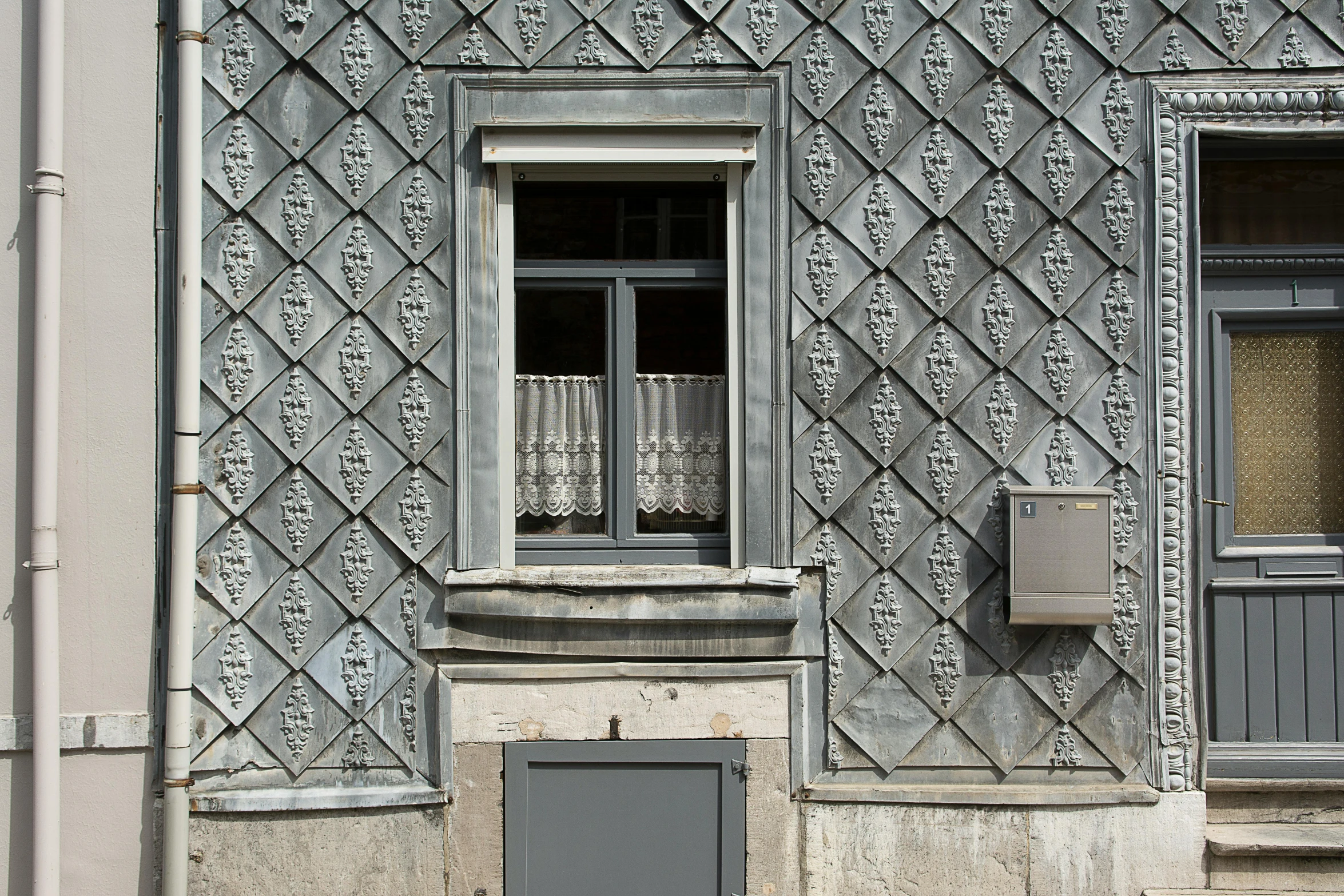 a black fire hydrant sitting in front of a building, an album cover, inspired by Károly Markó the Elder, baroque, tiles curtains, silver，ivory, flat grey color, metal cladding wall