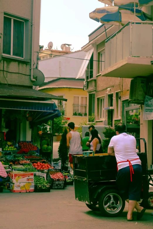 a group of people walking down a street next to a building, fruit, istanbul, gardening, day time