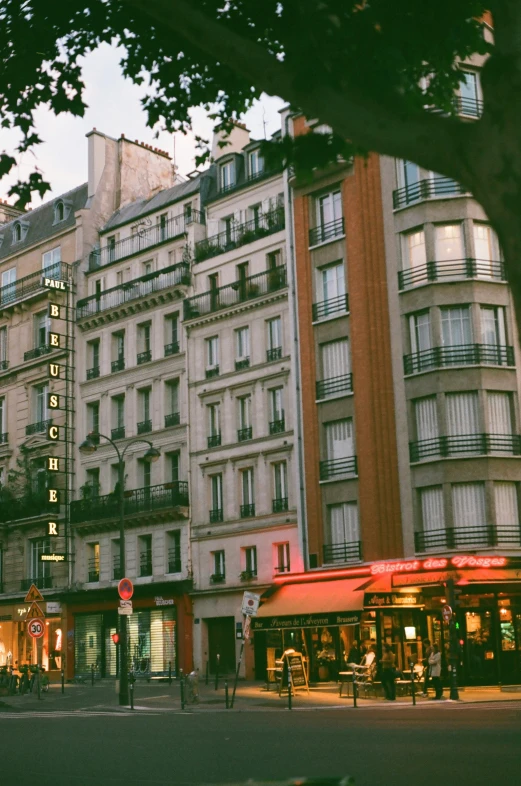 a city street filled with lots of tall buildings, a photo, paris school, soft evening lighting, storefront, lush surroundings, french nouveau