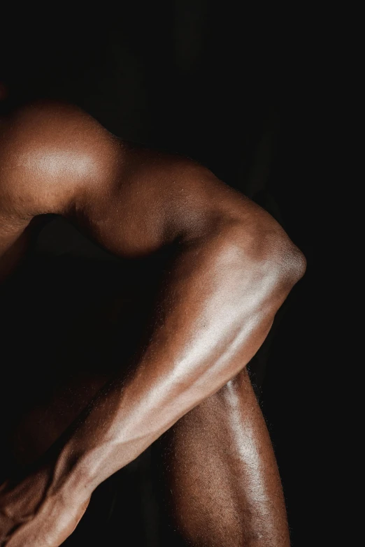 a man sitting on the ground with his hands on his knees, an album cover, inspired by Robert Mapplethorpe, pexels contest winner, renaissance, big biceps, dark brown skin, closeup of arms, “ sensual