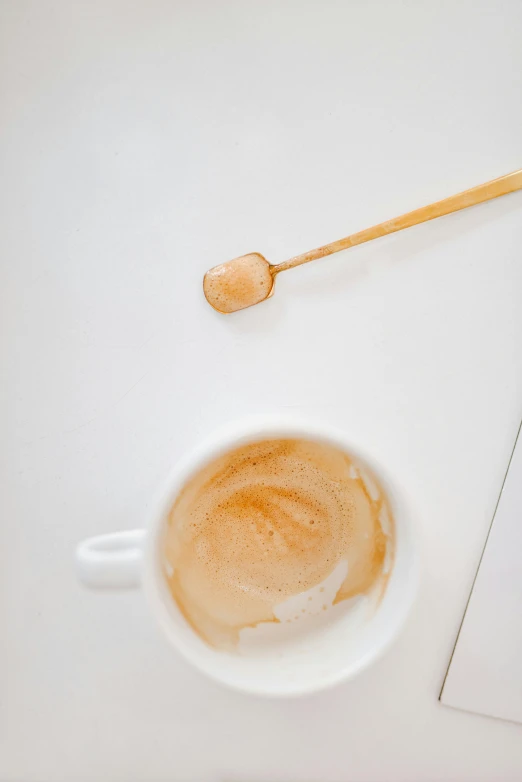 a cup of coffee and a spoon on a table, product image, light tan, white and orange, top - down photograph